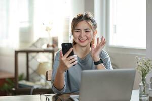 Mujeres de negocios independientes ropa casual usando una computadora portátil, llamada de trabajo, videoconferencia con el cliente en el lugar de trabajo en la sala de estar en casa. feliz joven asiática relajarse sentado en el escritorio hacer trabajo en internet. foto