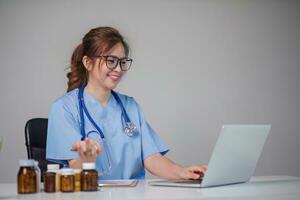 Young Asian doctor in a white medical uniform with a stethoscope using a lab computer and tablet to organize and classify medicines in preparation for administration to patients. photo