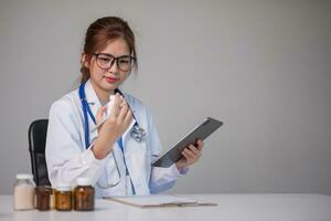 Young Asian doctor in a white medical uniform with a stethoscope using a lab computer and tablet to organize and classify medicines in preparation for administration to patients. photo