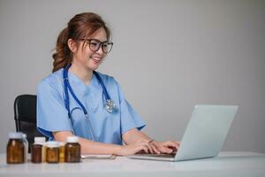 Young Asian doctor in a white medical uniform with a stethoscope using a lab computer and tablet to organize and classify medicines in preparation for administration to patients. photo