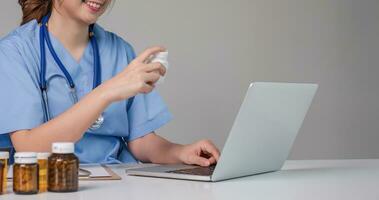 Young Asian doctor in a white medical uniform with a stethoscope using a lab computer and tablet to organize and classify medicines in preparation for administration to patients. photo