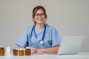 joven asiático médico en un blanco médico uniforme con un estetoscopio utilizando un laboratorio computadora y tableta a organizar y clasificar medicamentos en preparación para administración a pacientes foto