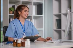 Beautiful Asian doctor smiling using laptop computer explaining detailed medical information online at hospital health medical concept. photo