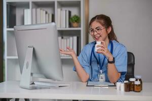 joven hermosa médico participación píldora botella explicando detalles acerca de medicina vía ordenador portátil en línea a clínica foto