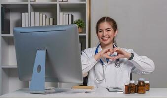 Beautiful asian woman wearing doctor uniform and stethoscope smiling in love doing heart symbol shape with hands. romantic concept. photo