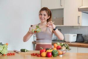 joven atlético mujer es preparando un sano orgánico vegetal ensalada en un moderno cocina a hogar. foto