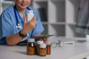 Hand of pharmacist holding plastic pill-bottle while showing it to one of patients during online consultation photo