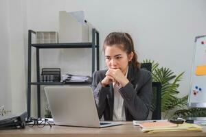 Confused Asian woman is seriously stressed about how to fix laptop screen problem. Serious Asian businesswoman worried focused on solving difficult computer tasks photo