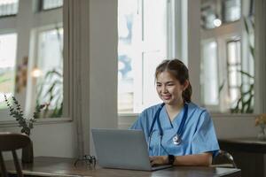 joven asiático dama médico en blanco médico uniforme con estetoscopio utilizando computadora ordenador portátil hablando vídeo conferencia llamada con paciente a escritorio en salud clínica o hospital. foto