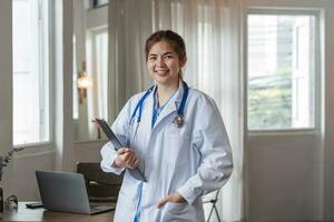 sonriente hembra médico participación un portapapeles con información y paciente cuidado documentos. y estetoscopio en el del doctor oficina en el hospital foto