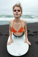 Woman surfer is lying on front on surfboard, leaning on hands and arching back, looking at camera photo