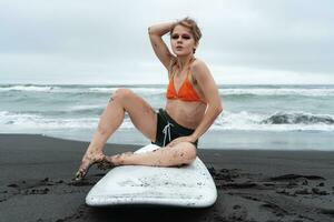 mujer tablista sentado en tabla de surf en arenoso playa en antecedentes de Oceano olas durante verano fiesta foto