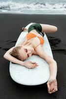 Female surfer is enjoying well deserved break on sandy beach, lying on surfboard with eyes closed photo