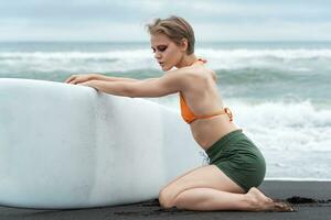 Female surfer, with her eyes closed, is kneeling and holding her surfboard during summer vacation photo