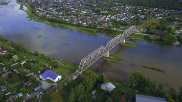 Top view of beautiful landscape of river and town with bridge. Clip. Reflection of sky in river with beautiful bridge on sunny summer day. Landscape with suspension bridge over river in modern town in photo