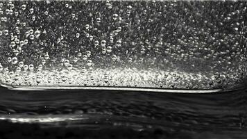 Close-up of small bubbles floating in the glass filled with sparkling water on the dark background. Monochrome photo