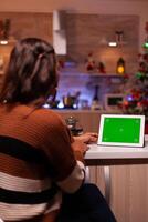 Caucasian adult watching green screen technology on tablet sitting at kitchen counter. Young woman using digital chroma key concept for background template, mockup gadget app on display photo