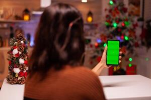 Festive person holding smartphone with green screen for modern technology on mockup template. Caucasian young woman watching digital device with chroma key to view background design photo