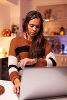 Upset woman having to work on christmas eve night using business laptop technology at festive home. Young adult on virtual network for project deadline feeling sad about missing party photo