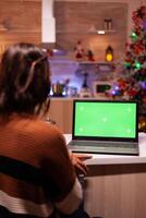 Caucasian adult looking at laptop computer with green screen modern technology for mockup template gadget. Young festive woman using device for digital chroma key isolated display photo