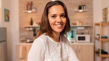 joven mujer de negocios sonriente a cámara tarde a noche trabajando en proyecto. concentrado empresario en hogar cocina utilizando cuaderno durante tarde horas en el noche. foto