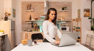Tired businesswoman working overtime late at night using laptop in home office. Concentrated entrepreneur in home kitchen using notebook during late hours in the evening. photo