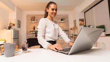 Busy businesswoman comunicating with potential client at night using laptop. Concentrated entrepreneur in home kitchen using notebook during late hours in the evening. photo