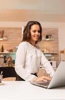 Corporate worker looking at laptop desktop working at important deadline. Concentrated entrepreneur in home kitchen using notebook during late hours in the evening. photo