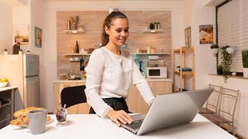 Freelance businesswoman sitting at desk in home working on laptop. Concentrated entrepreneur in home kitchen using notebook during late hours in the evening. photo