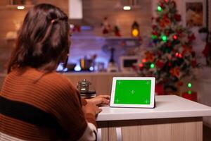 Young person watching green screen technology on tablet in kitchen at home. Caucasian woman using digital chroma key concept for background template, mockup gadget app on virtual display photo
