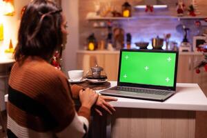 Caucasian adult looking at laptop computer with green screen modern technology for mockup template gadget. Young festive woman using device for digital chroma key isolated display photo