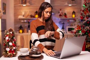 Angry person working on christmas eve night using laptop computer technology at festive home. Young woman on virtual network for business project, upset adult about wasting time photo