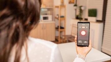 Woman controlling lights with app on her phone sitting at desk in kitchen. Person in apartment holding telephone with touchscreen and app for lights. photo