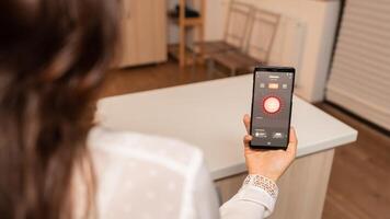 Woman in home kitchen using phone app to remotely control lighting system. Person in apartment holding telephone with touchscreen and app for lights. photo