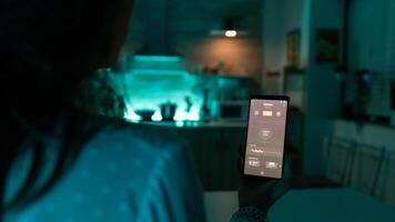 Woman in home dark room using automation app for lighting. Person in apartment holding telephone with touchscreen and app for lights. photo