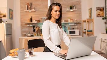 Woman in home kitchen during night hours working on laptop to finish deadline for work. Concentrated entrepreneur in home kitchen using notebook during late hours in the evening. photo
