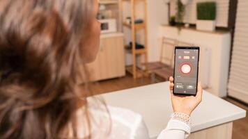 Woman in kitchen using voice controll on phone to change lighting. Person in apartment holding telephone with touchscreen and app for lights. photo