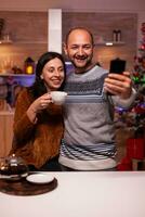 Smiling family taking selfie using smartphone enjoying christmas time standing in xmas kitchen. Happy joyful family celebrating winter holiday season. New year festive season photo