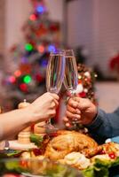 Closeup of couple clinking glass of wine during christmas dinner sitting at dining table in xmas decorated kitchen. Happy romantic family celebrating christmas holiday together enjoying winter season photo