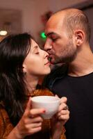 Portrait of happy boyfriend kissing girlfriend on nose celebrating christmas holiday together spending time together in xmas decorated kitchen. Joyful couple enjoying winter season. photo