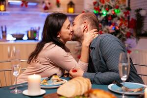 Happy couple kissing in xmas kitchen after marriage proposal enjoying christmas holiday sitting at dinning table. Couple enjoying spending time together during winter season photo