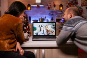 Happy family celebrating christmas holiday with remote friends during online videocall meeting conference in xmas decorated kitchen. Joyful couple enjoying spending time together during winter season photo