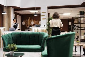 Hotel concierge checking record forms in lounge area at reception, reviewing registration files and booking bureaucracy. Female manager working on providing excellent service for guests. photo