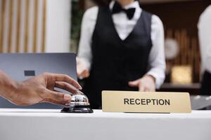 Tourist using service bell at front desk, ringing bell to talk to receptionist in lobby and check in. Hotel guest at reception counter receiving luxury assistance with room accommodation. Close up. photo