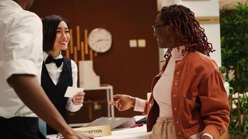 Happy receptionist handing relaxed smiling newlywed couple room access key card during check in process. Cheerful tourists and professional hotel staff chatting in resort lobby photo