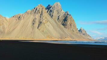 Vestrahorn mountains on arctic peninsula with natural black sand beach and beautiful skyline, sightseeing adventure. Ocean coastline shore and hills forming majestic landscape. Handheld shot. photo