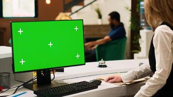 Hotel staff working with pc greenscreen at reception, talking to tourists upon their arrival. Front desk worker using blank copyspace template with isolated display, doing check in. Tripod shot. photo