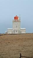 Icelandic Dyrholaey historical tower with beautiful lighthouse on mainland to help guide sailors. Navigation tower with light used near icelandic cliff coastline, arctic shore ocean guidance. photo