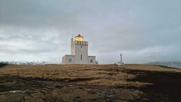 Dyrholaey beautiful lighthouse on icelandic peninsula with frozen fields and guidance building near ocean coastline. Amazing colorful tower used for navigation as beacon of light in iceland. photo