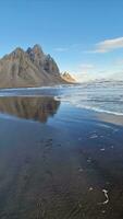 Stone mountain crests meeting the ocean in fantastic icelandic environment with natural black sand beach. Nordic stokksnes peninsula with vestrahorn mountain chain and beachfront, sightseeing. photo